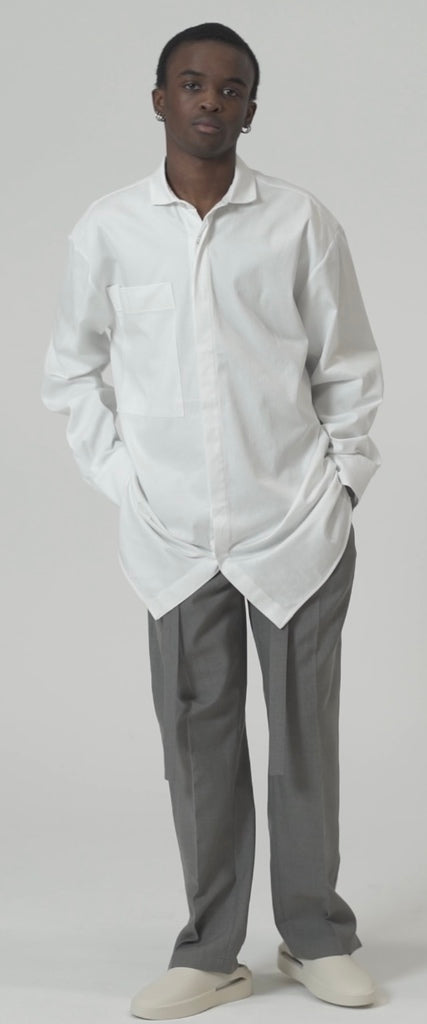 Model wearing an oversized cotton blend shirt in white with oversized pocket, paired with gray trousers.