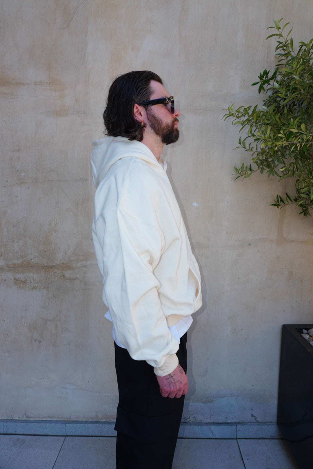 Man wearing cream 'Imagine' screen print logo hoody, showcasing relaxed fit and kangaroo pocket, side profile.