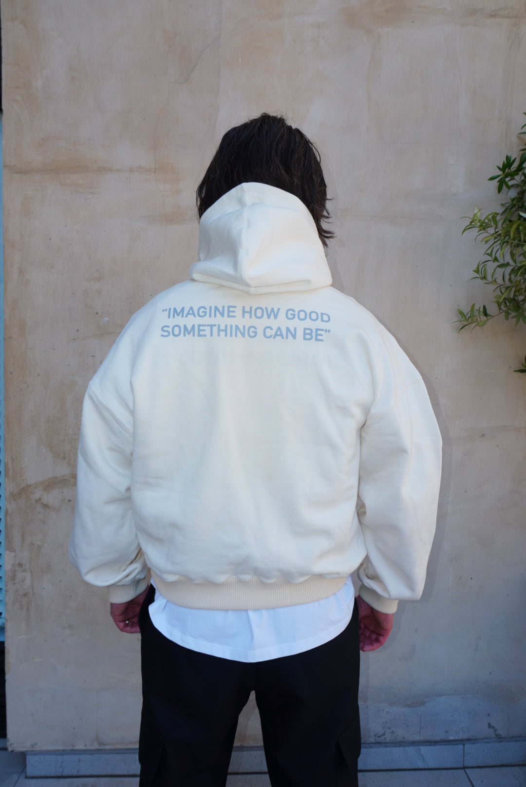 Cream relaxed fit hoody with grey screen print logo on back, worn by a model, perfect for casual style and comfort.