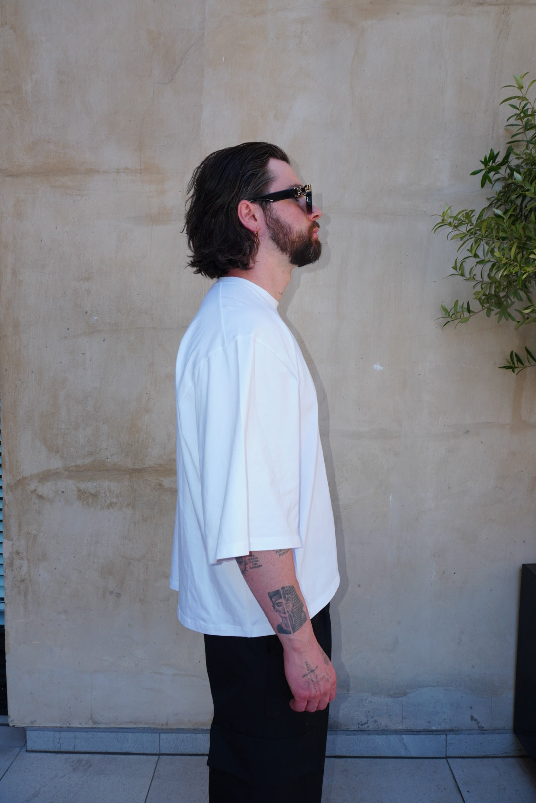 Man in side profile wearing white boxy fit tee with slightly lengthened sleeves and black screen print logo.