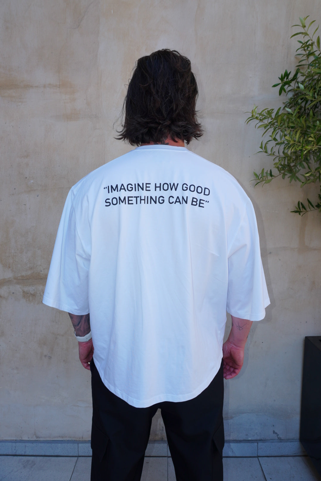 Model wearing back of 'Imagine' Screen Print Logo Boxy Tee in white with black text. Casual and stylish design.