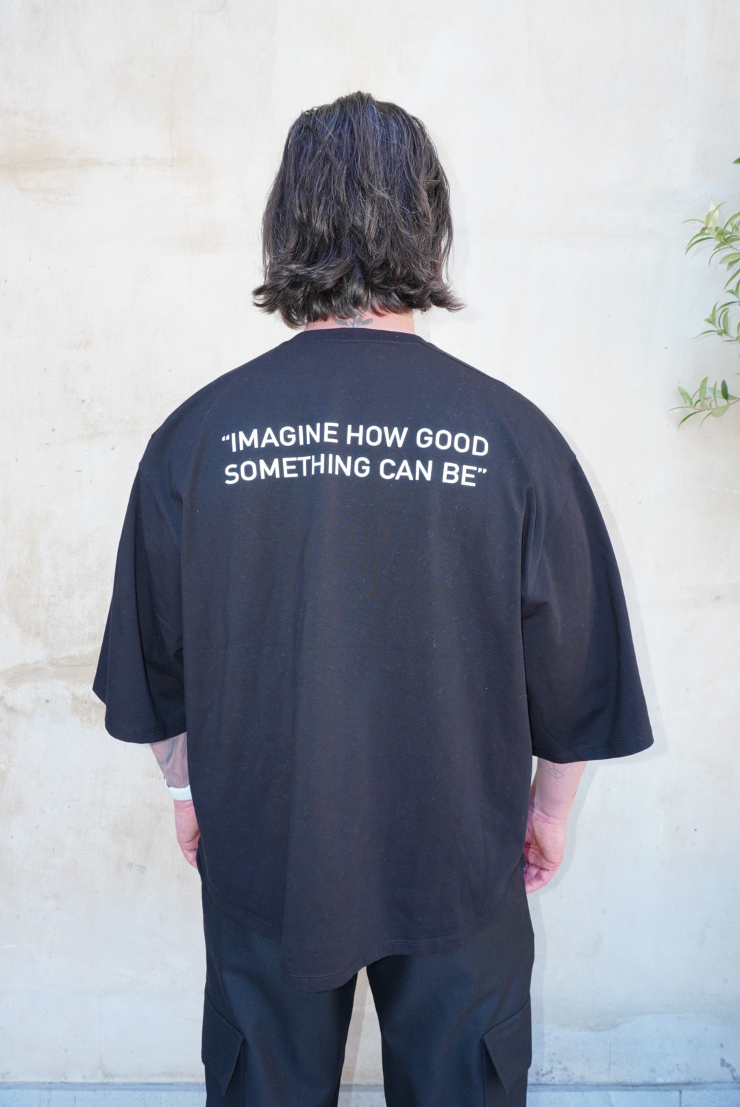 Black boxy fit tee with white screen printed logo on back, featuring the phrase 'IMAGINE HOW GOOD SOMETHING CAN BE'.