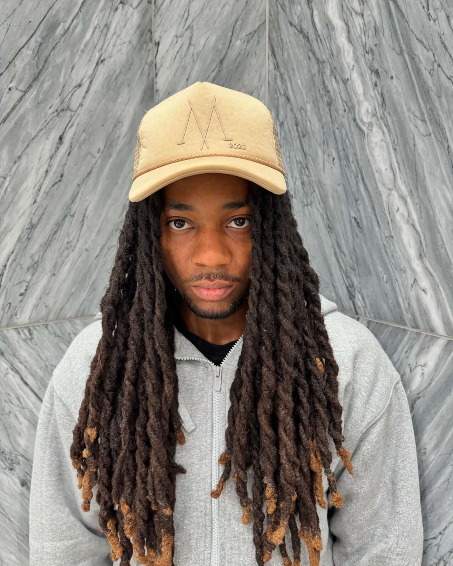 Man wearing a taupe foam front trucker cap with puff print logo, featuring snapback closure, against a marble background.
