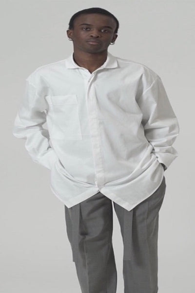 Model wearing an oversized cotton blend shirt in white with an oversized pocket, styled with grey pants.
