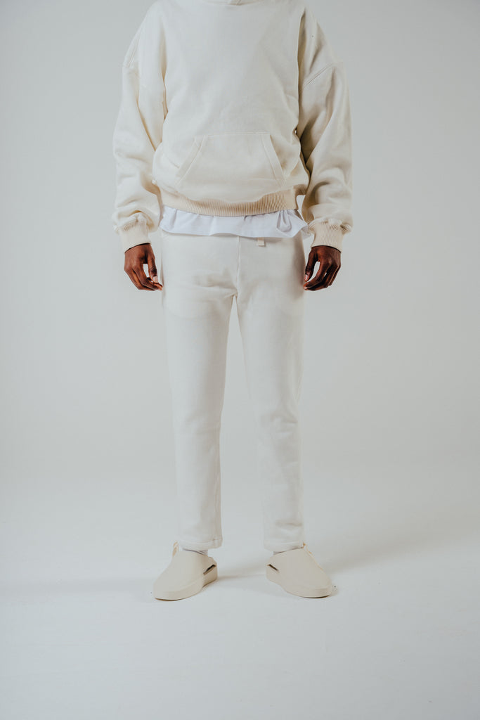 Relaxed fit cropped leg jogger in cream, made from a fleeceback cotton blend, styled with a matching hoodie and slip-on shoes.