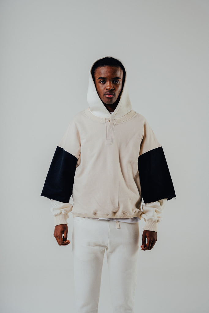 Model wearing a cream and black cropped boxy fit Henley sweatshirt with a hood and contrast sleeves.