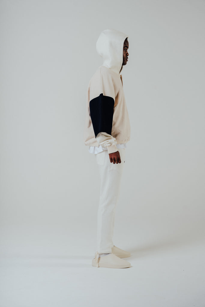 Model wearing cream and black cropped hoodie with white pants, showcasing side profile against a neutral background.
