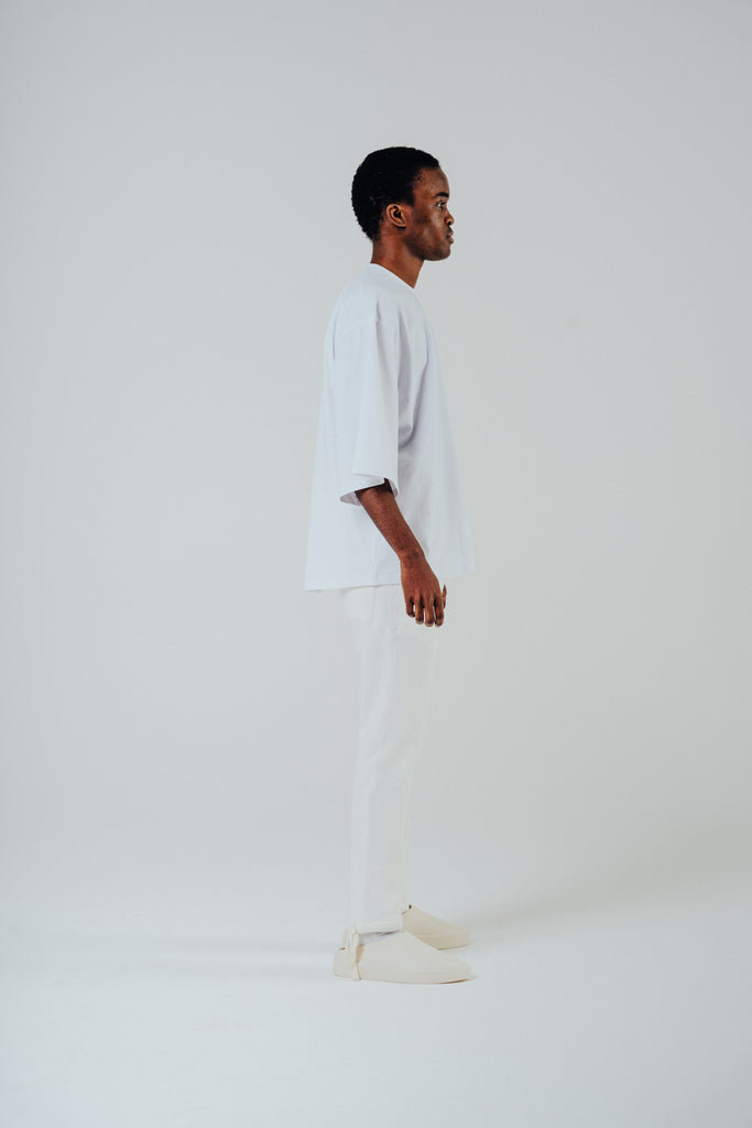 Model in profile wearing a relaxed cropped tee in white, showcasing a cotton blend fabric and slightly lengthened sleeves.