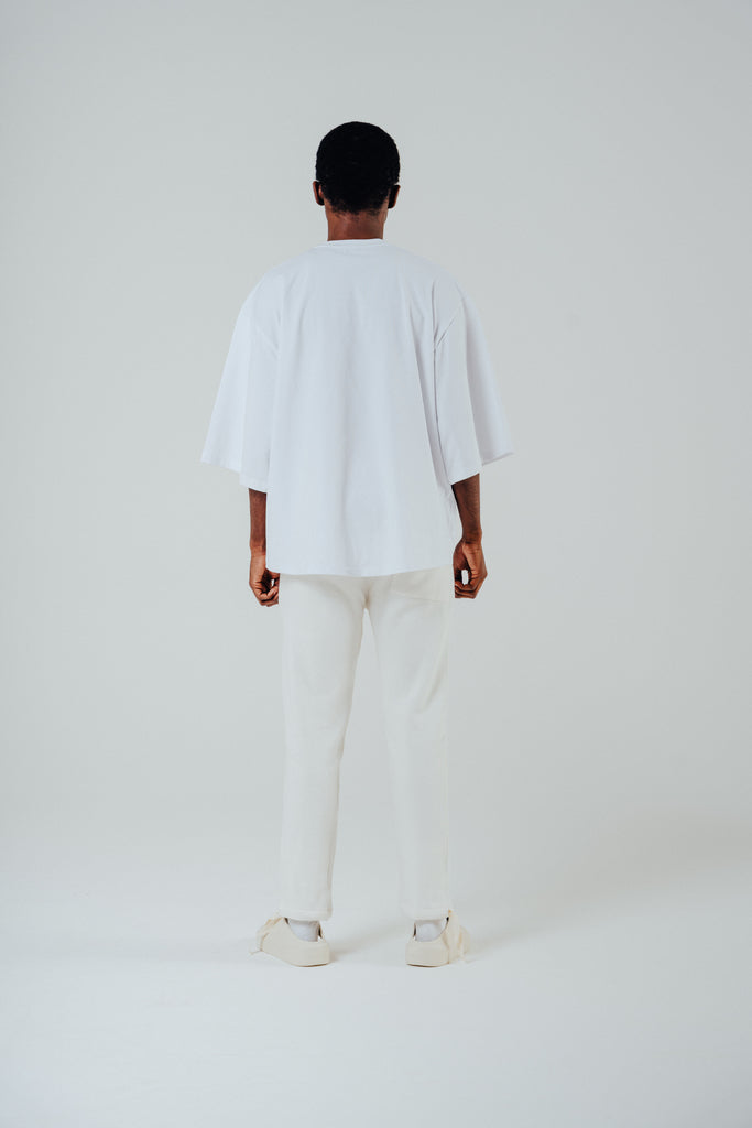 Model wearing a relaxed cropped fit cotton tee in white, showcasing the back view and slightly lengthened sleeves.