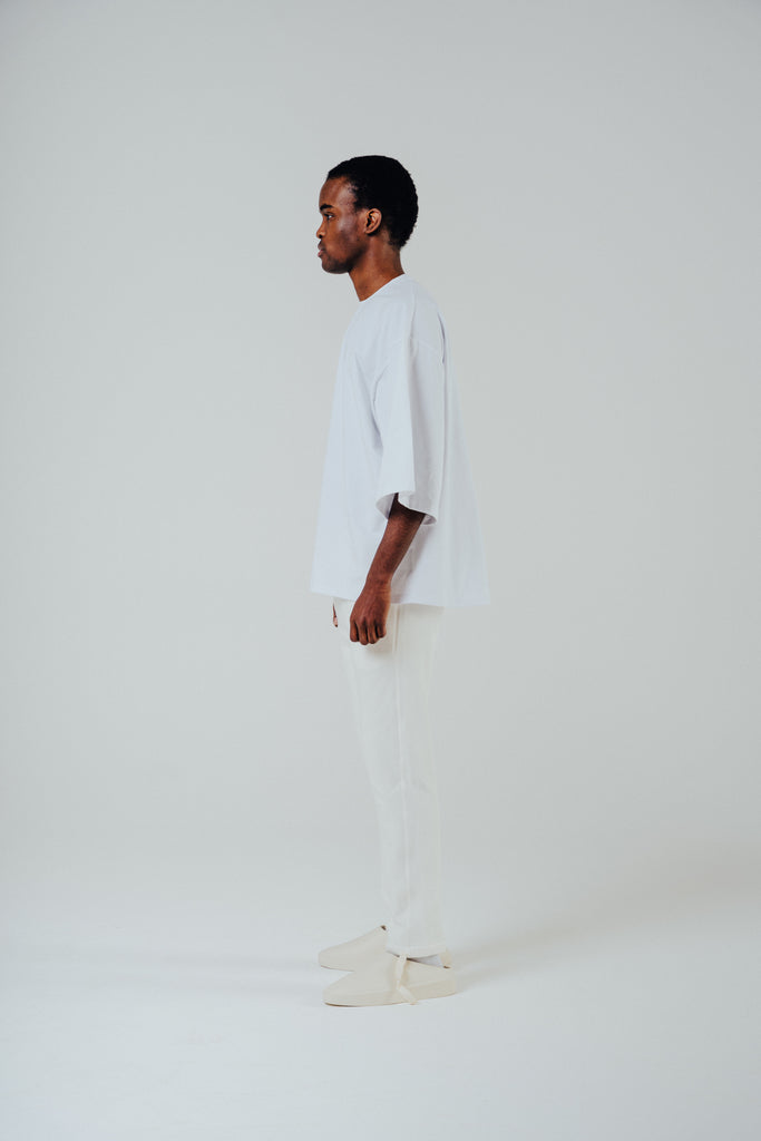 Model in relaxed cropped fit cotton tee in white, showcasing slightly lengthened sleeves and soft cotton blend.