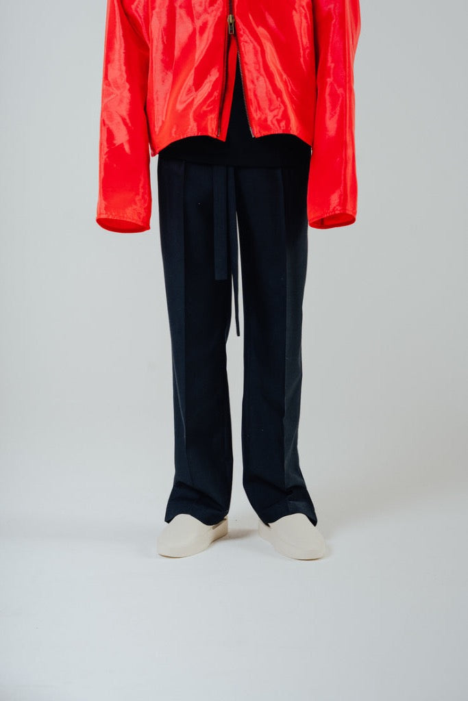 Tailored rope belt trousers in black paired with a bright red jacket and light footwear, showcasing a relaxed fit style.