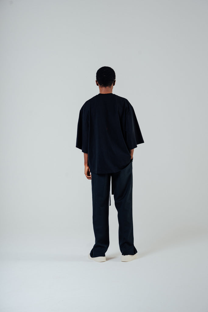 Model showing the back view of tailored rope belt trousers in black with relaxed fit and loose top, styled for a modern look.