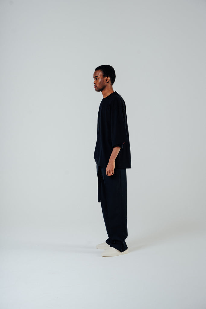 Relaxed cropped fit tee in black on a model, showcasing slightly lengthened sleeves and a cotton blend fabric.