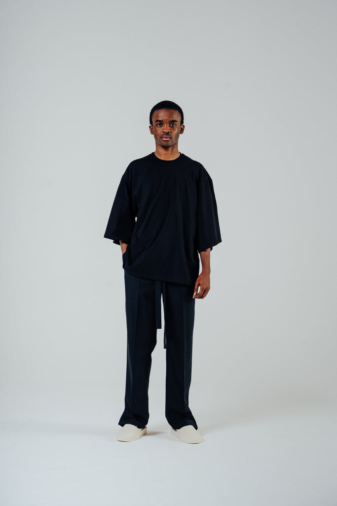 Model wearing a relaxed cropped tee in black with slightly lengthened sleeves, paired with matching black pants.
