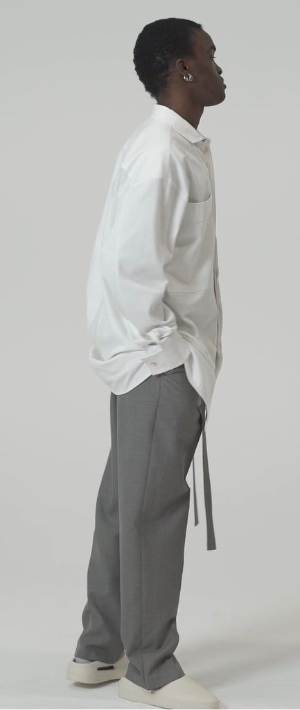 Model showcasing tailored rope belt trousers in grey with a relaxed fit and popper button at ankle, paired with a white shirt.