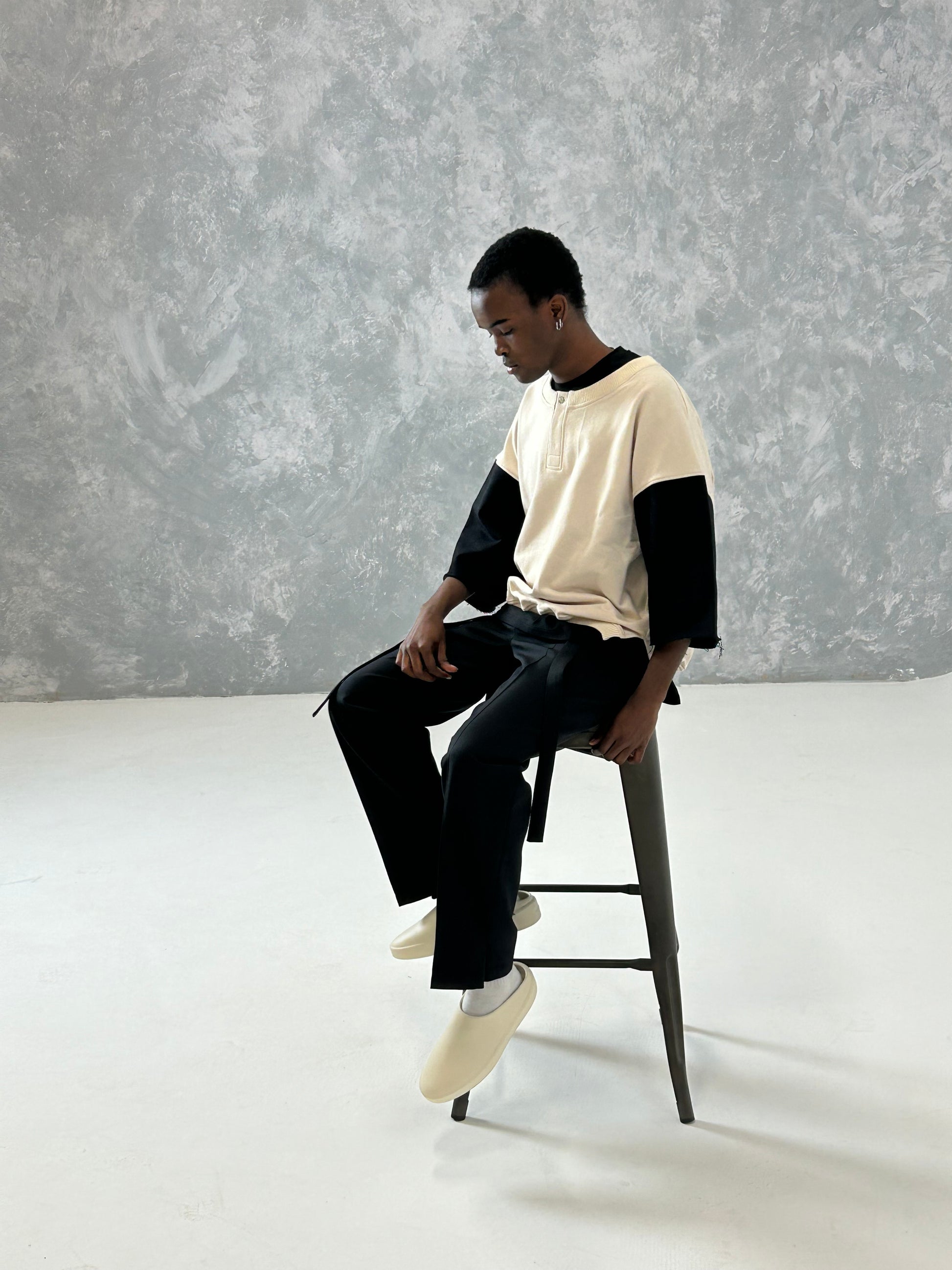 Model wearing a cropped boxy fit henley top in cream and black, styled with black pants and light shoes.