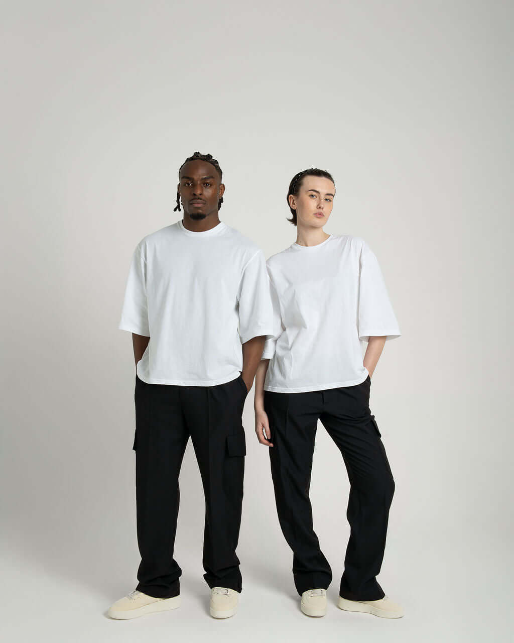 Boxy cropped tee in white on male and female models, showcasing soft cotton fabric and relaxed fit, styled with black pants.