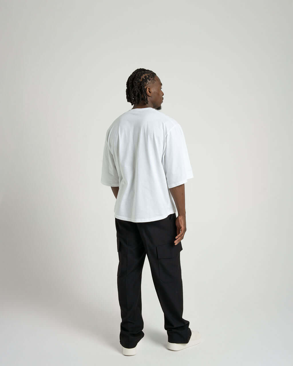 Model wearing a boxy cropped white tee from the back, paired with black pants, showcasing soft, luxurious cotton.