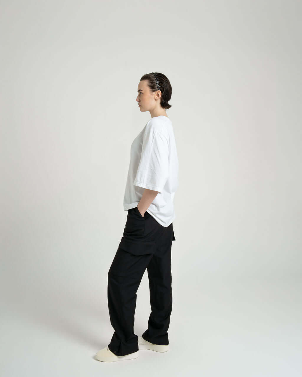 Model wearing black tailored wool cargo trousers with relaxed fit and envelope pockets, paired with a white oversized t-shirt.