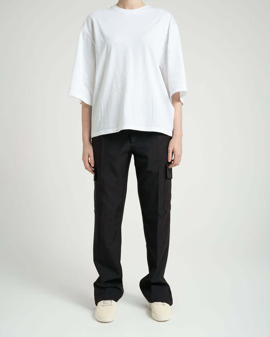 Model wearing a white oversized t-shirt and black tailored cargo trousers with relaxed fit and envelope pockets.