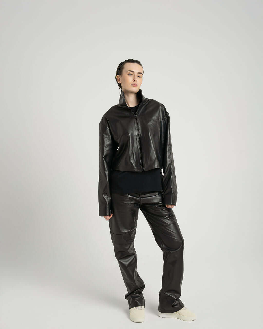 Model wearing a cropped zipped black leather jacket with fitted pants, showcasing a stylish and contemporary outfit.
