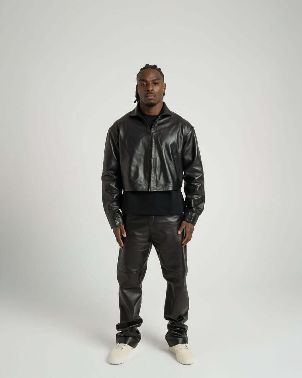 Model in a cropped zipped black leather jacket paired with matching pants, showcasing a stylish and modern look.