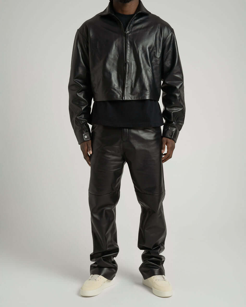 Model wearing black leather trousers with flare ankle and matching cropped jacket, showcasing relaxed fit and style.