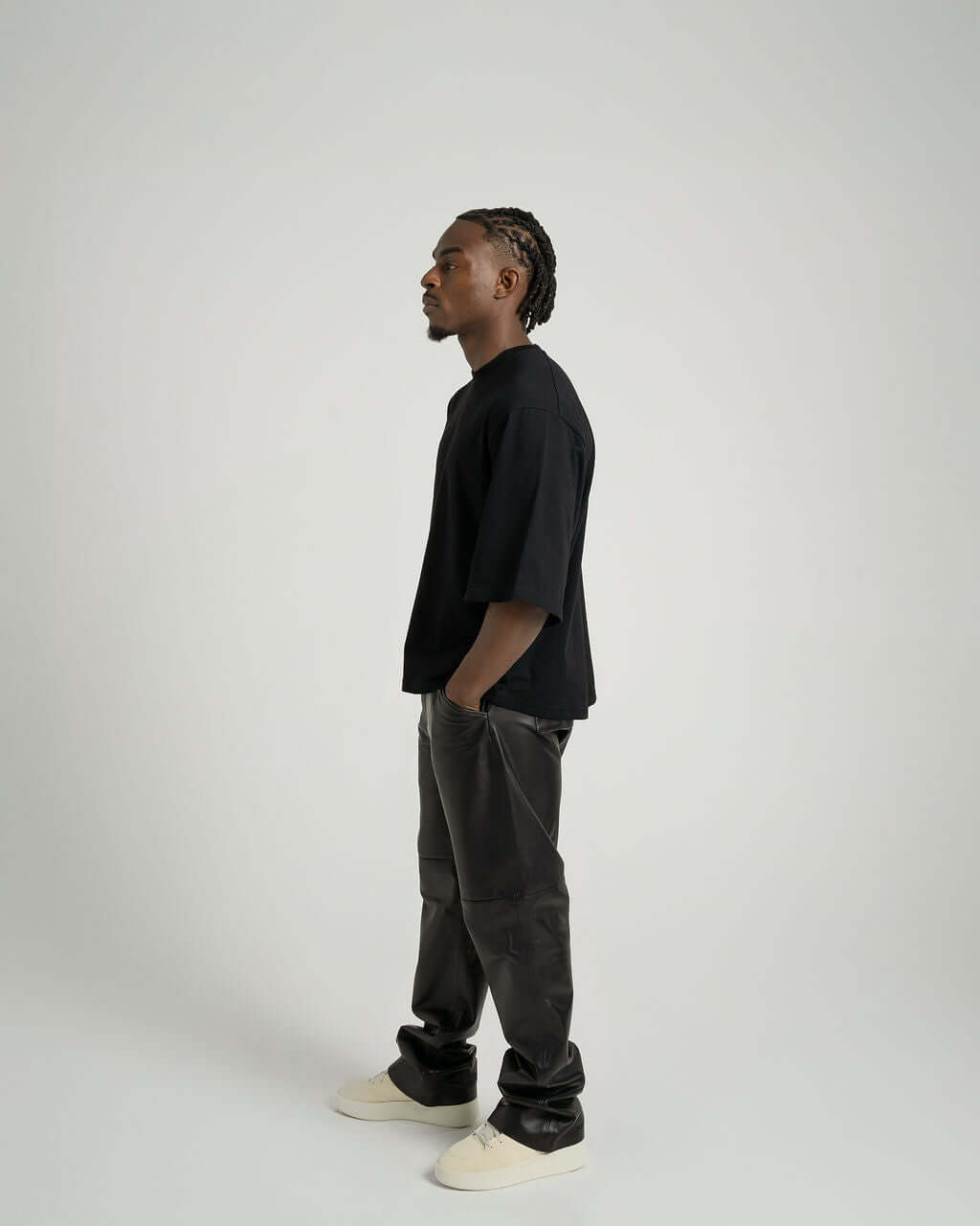 Model wearing a black boxy cropped tee with slightly lengthened arms, paired with dark pants, showcasing side profile.