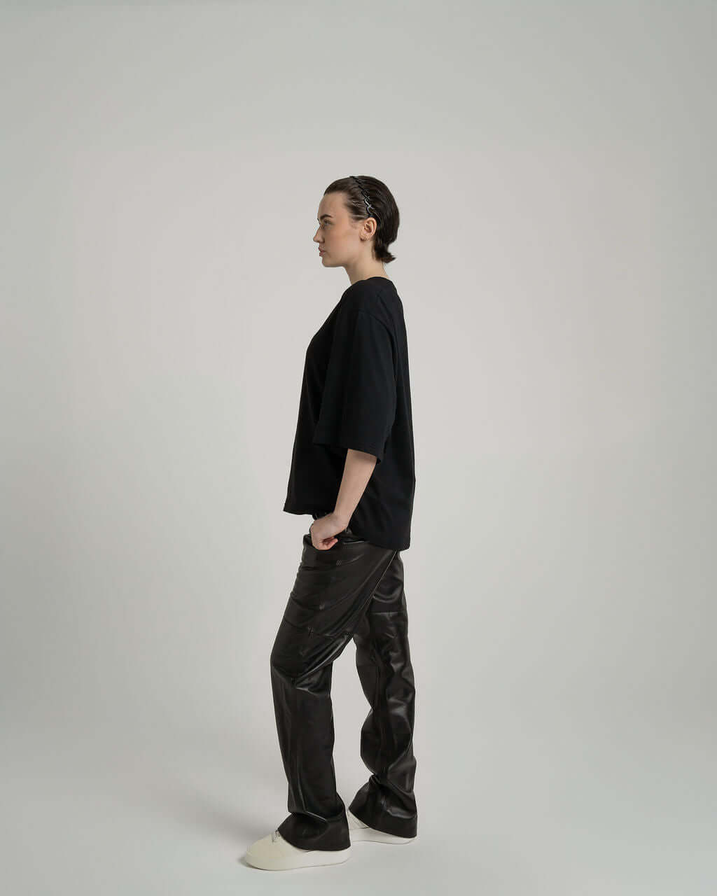 Model wearing a black boxy cropped tee paired with black pants, showcasing a stylish side view in a minimalistic setting.