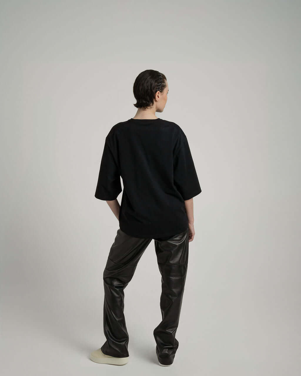 Back view of a model wearing a Boxy Cropped Tee in Black, paired with stylish black trousers, showcasing a relaxed fit.