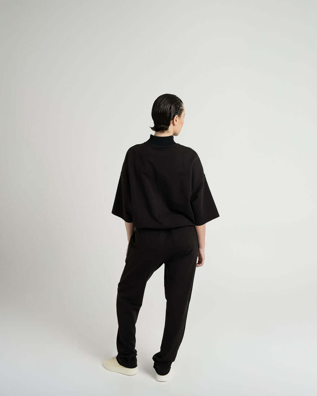 Woman wearing a black 3/4 sleeve mock neck terry sweatshirt with oversized fit, seen from the back.