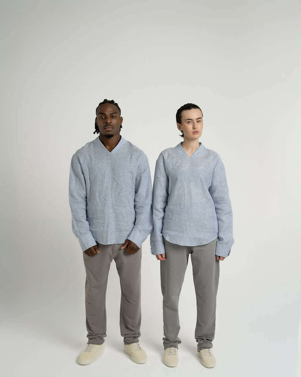 Two models wearing a blue and white striped linen long sleeve pullover shirt in relaxed fit with v-neck and gray pants.