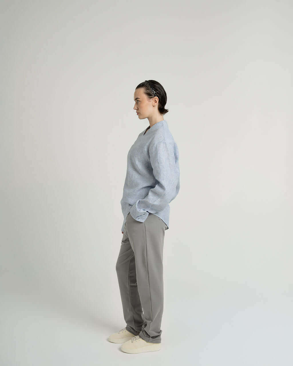 Side view of a model wearing a striped blue and white linen long sleeve pull over shirt with v-neck and relaxed fit.