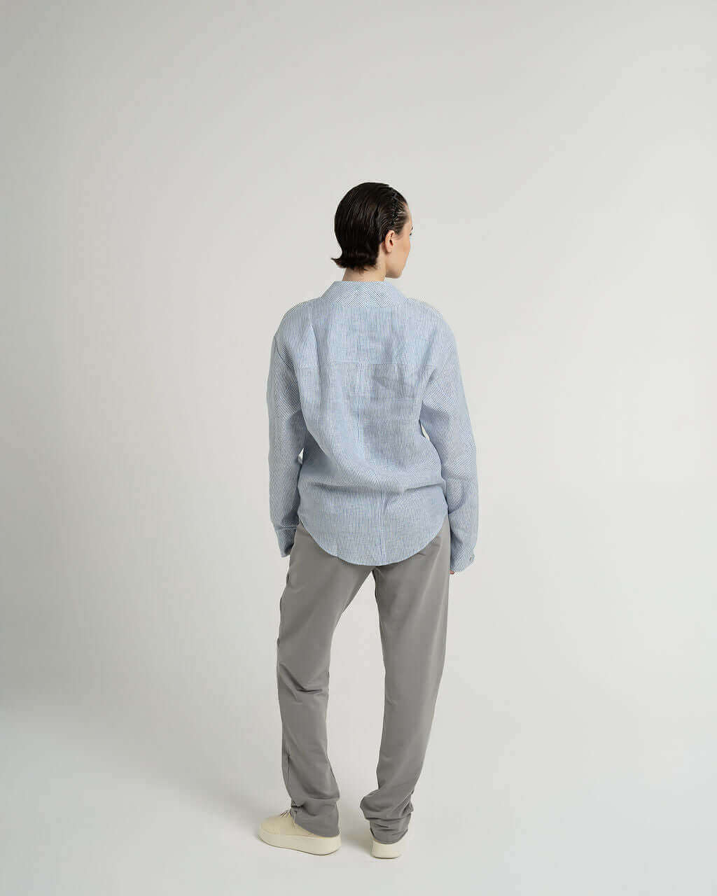 Blue and white striped linen long sleeve shirt with relaxed fit and twisted seams, worn by model from the back.
