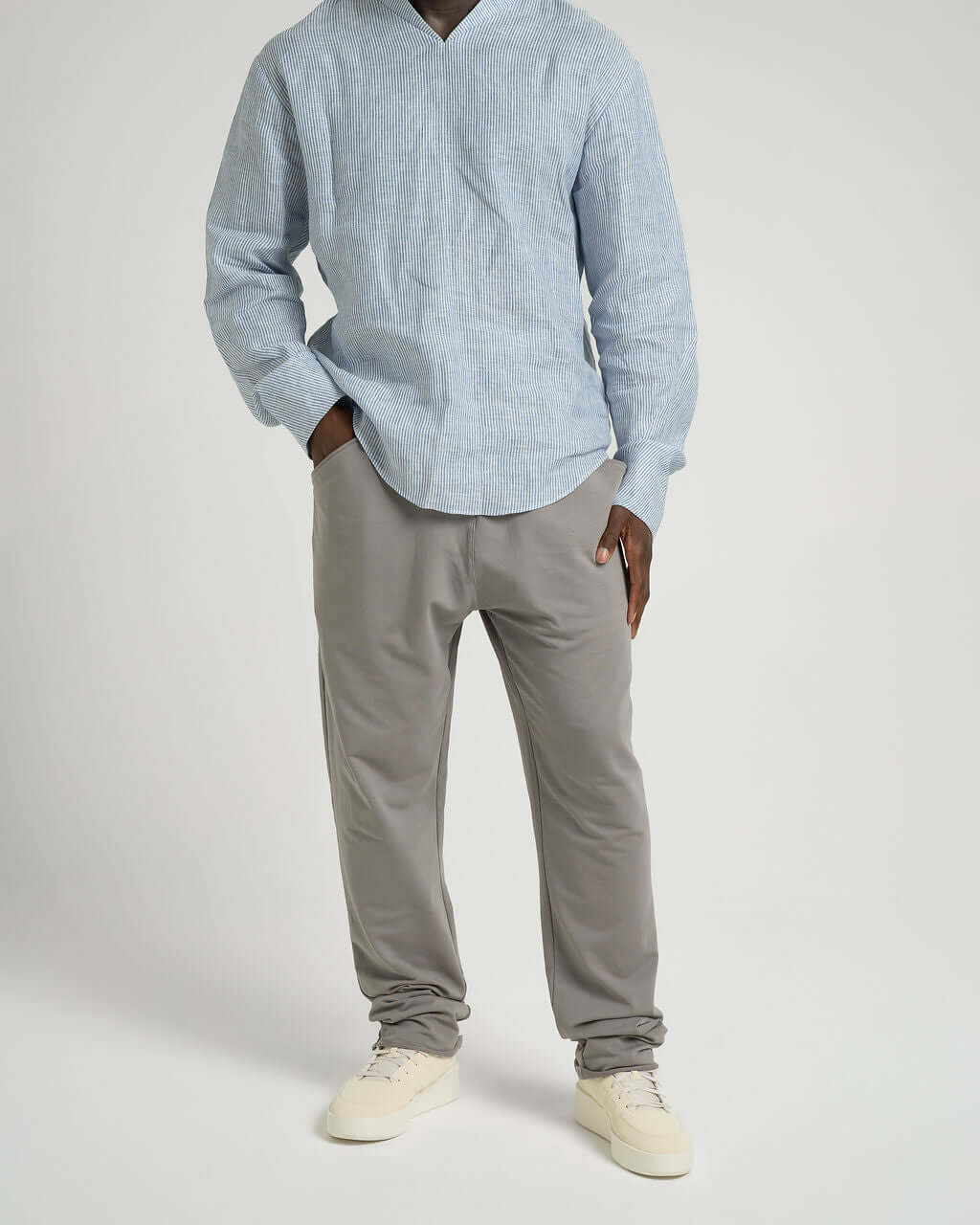 Man wearing grey French terry cotton trousers with a blue linen shirt and beige sneakers.