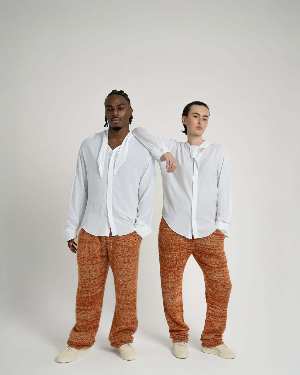 Two models showcasing a white viscose neck tie collar shirt styled open and tied, paired with relaxed pants.