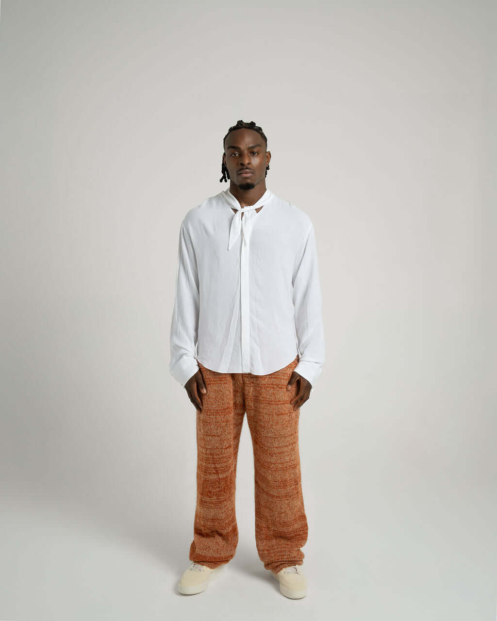 Model wearing a white viscose shirt with neck tie collar and relaxed fit pants, showcasing versatile styling options.