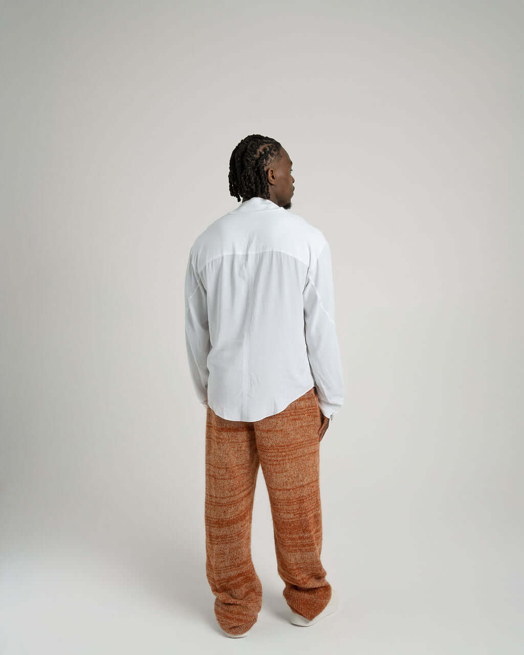 Back view of model wearing a white viscose shirt with neck tie collar and relaxed fit pants, showcasing styling options.
