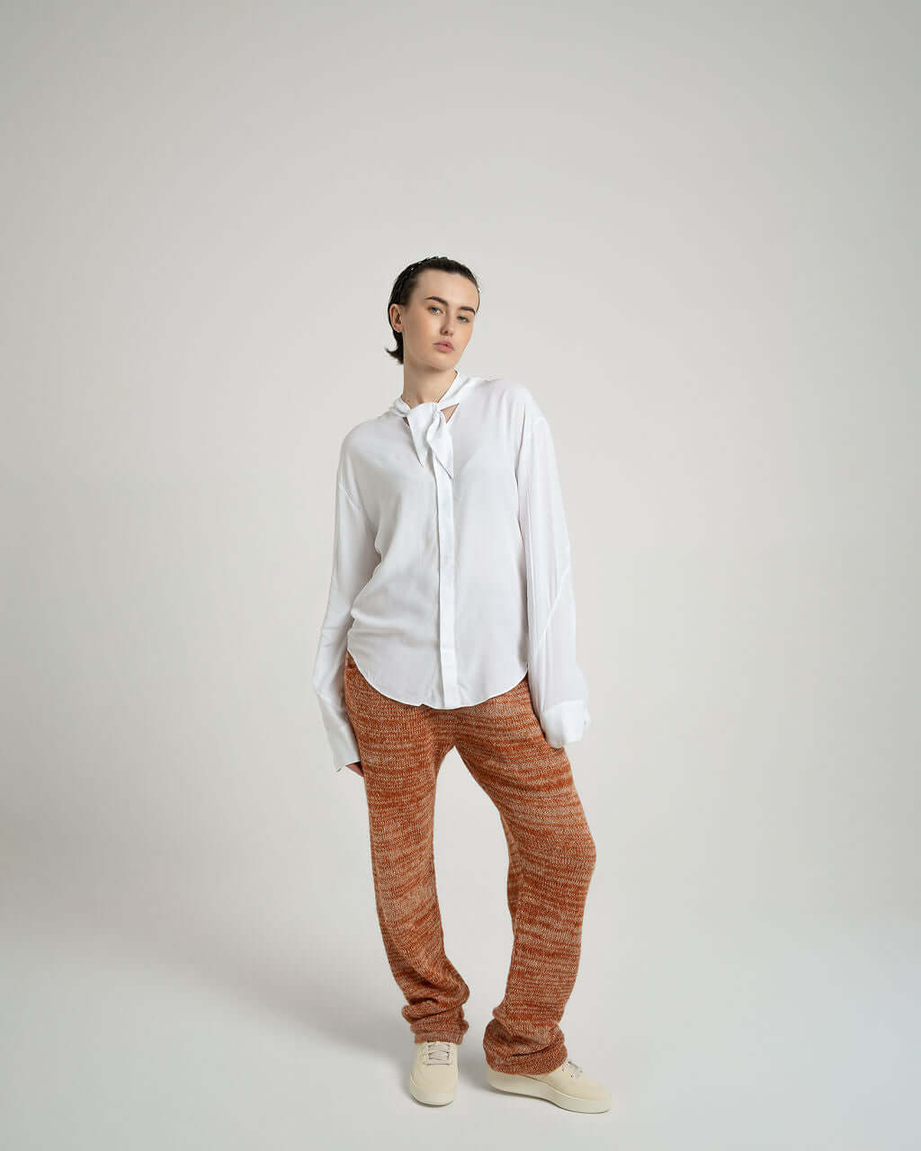 Model wearing a white viscose shirt with a neck tie collar, paired with orange patterned pants, showcasing relaxed fit style.