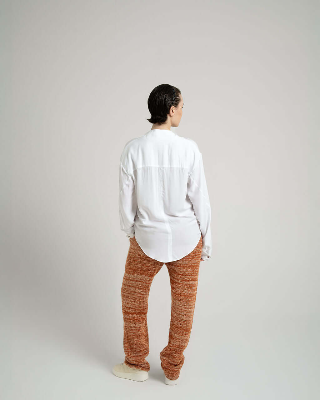 Model wearing a white viscose shirt with neck tie collar, styled with relaxed orange pants, showcasing a back view.