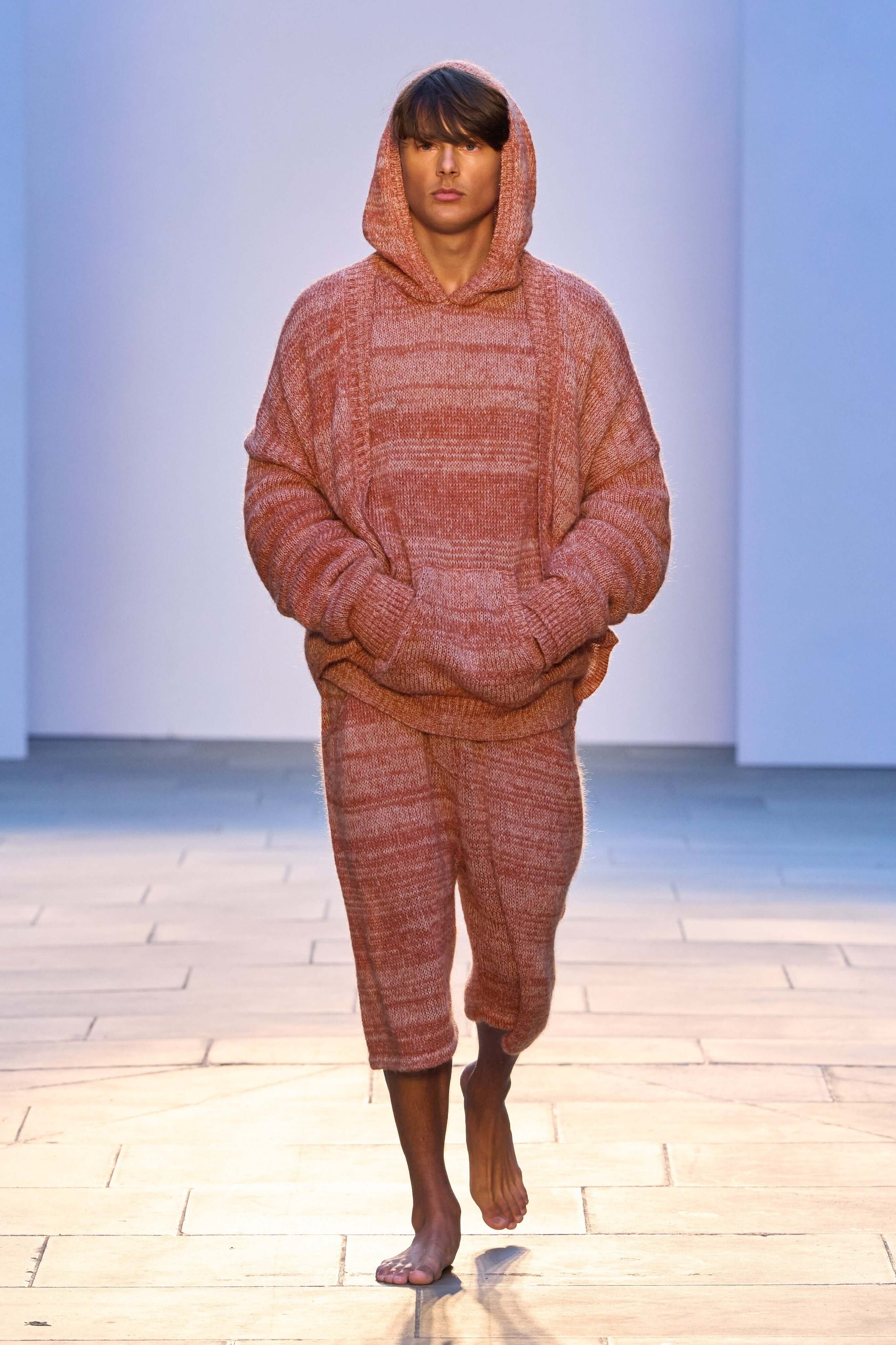 Model wearing oversized hooded knitwear set in warm tones, showcasing a relaxed fit and cozy style.