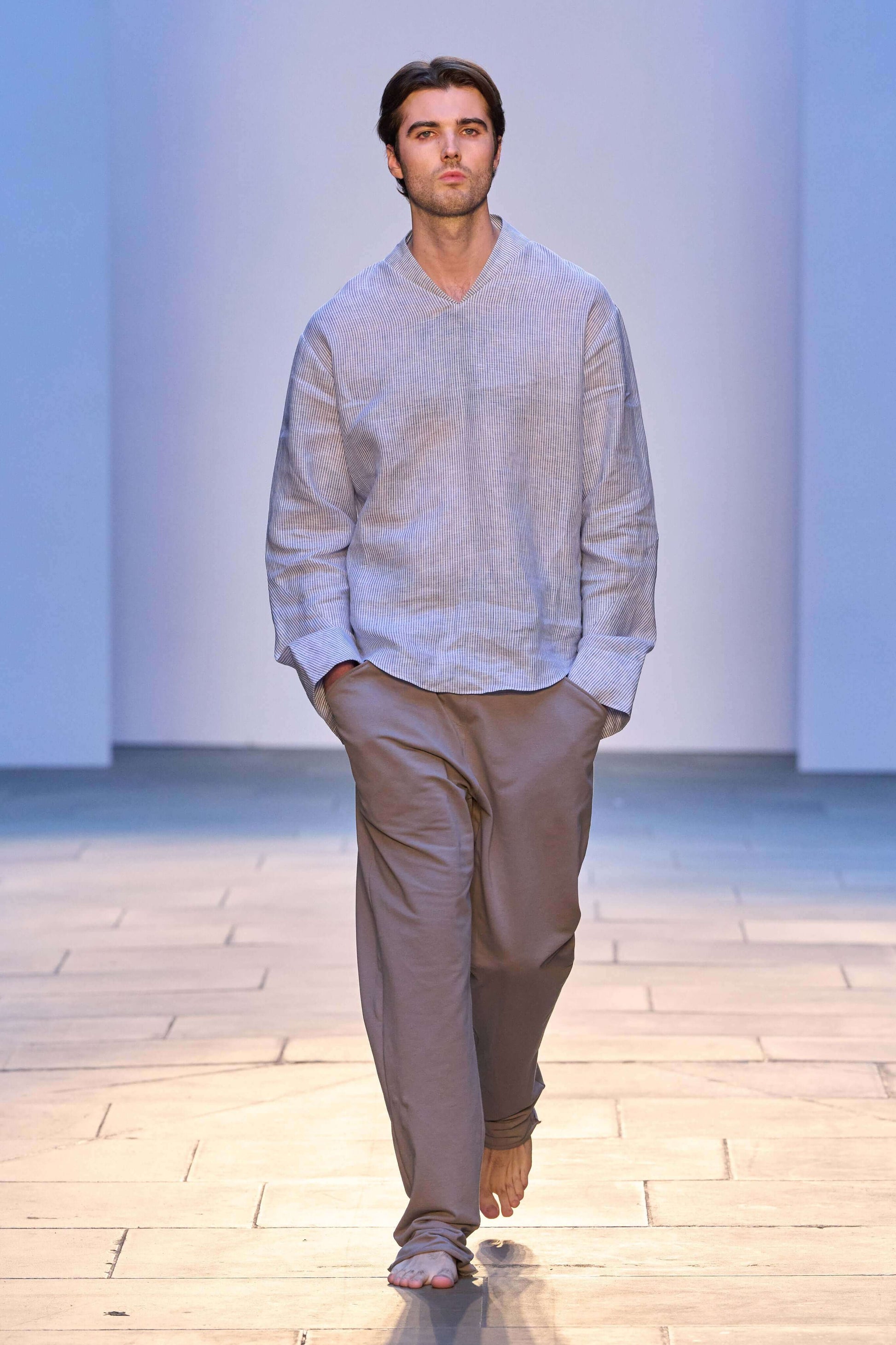 Model showcasing a relaxed blue and white striped linen long sleeve v-neck shirt during a fashion show.