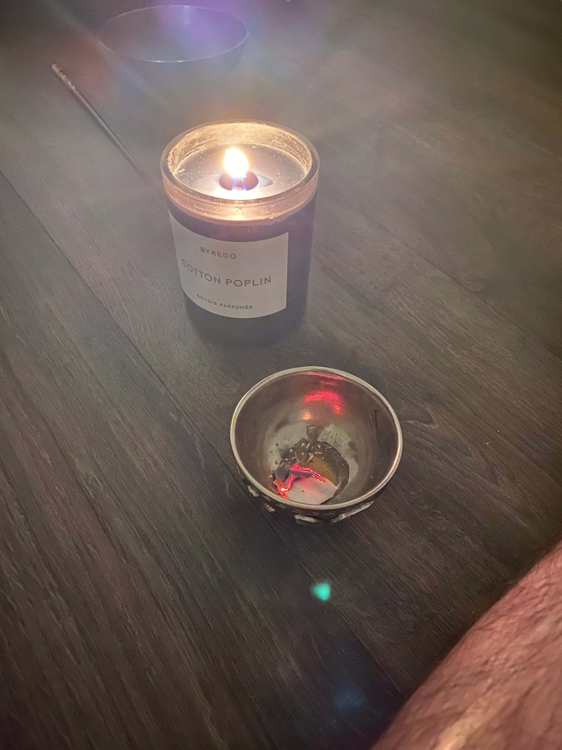 A lit candle labeled 'Cotton Poplin' next to a small bowl on a wooden surface, creating a warm ambiance.